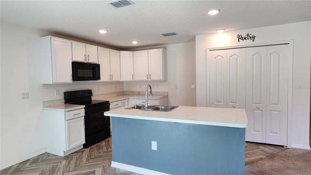 A kitchen features white cabinets, a black stove, a center island, and a pantry closet — 832 SORREL STREET NW, PALM BAY, FL