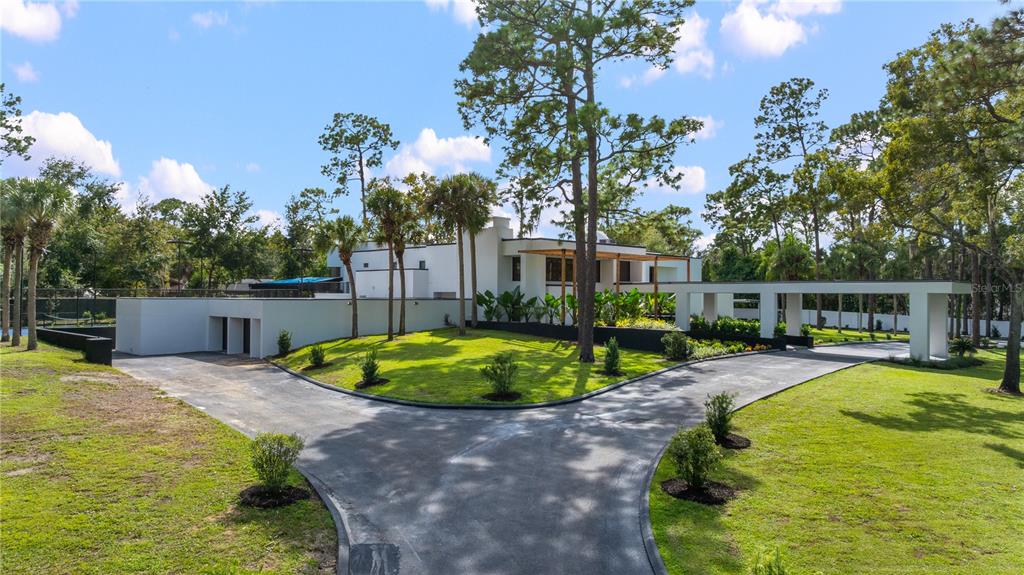 A modern white house with a split driveway and a covered walkway sits among trees — 808 SWEETWATER CLUB BOULEVARD, LONGWOOD, FL