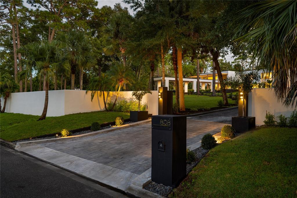 A paved driveway leads through a gated entrance toward a modern house surrounded by trees — 808 SWEETWATER CLUB BOULEVARD, LONGWOOD, FL