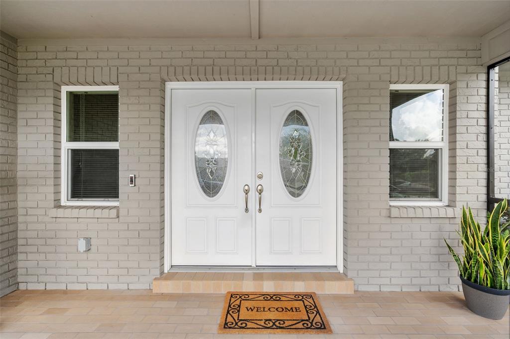 A white double front door with oval glass inserts sits between two windows on a brick-walled porch — 4029 BELL GRANDE DRIVE, VALRICO, FL