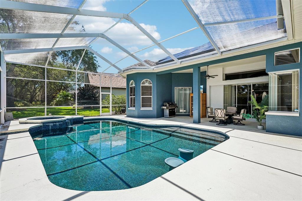 A screened-in patio features a swimming pool with a spa and outdoor dining area — 9039 WATERASH LANE N, PINELLAS PARK, FL