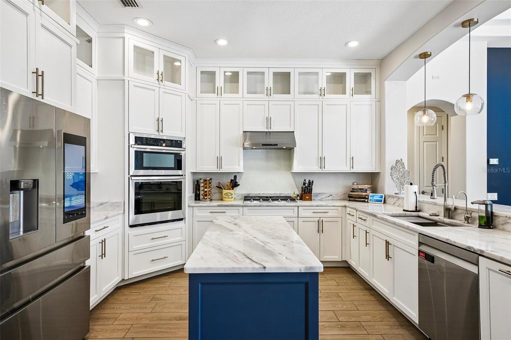 A modern kitchen features white cabinetry, a blue island, stainless steel appliances, and marble countertops — 9039 WATERASH LANE N, PINELLAS PARK, FL