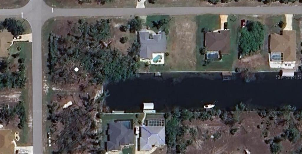 This aerial view shows a vacant lot next to a canal and several residential homes — 10394 SUNBURY DRIVE, PORT CHARLOTTE, FL
