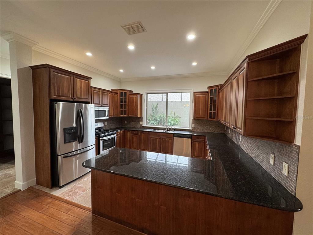 A kitchen features dark wood cabinets, black granite countertops, stainless steel appliances, and tile flooring — 1701 SE 28TH STREET, OCALA, FL