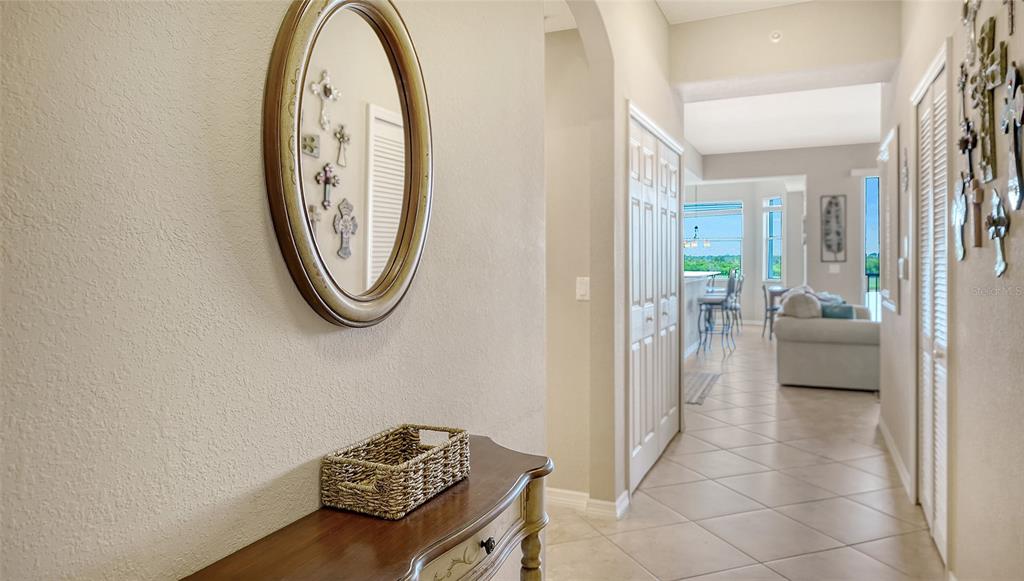 A hallway with a console table and mirror leads to an open-concept living area — 7705 GRAND ESTUARY TRAIL UNIT 207, BRADENTON, FL