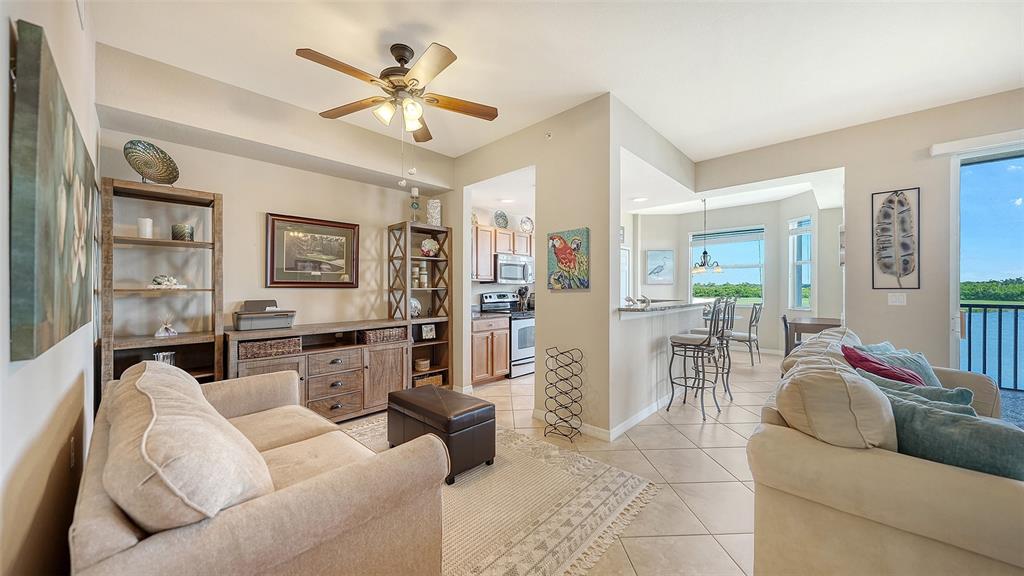 A living room with a beige sofa, ceiling fan, and an open view to the kitchen — 7705 GRAND ESTUARY TRAIL UNIT 207, BRADENTON, FL