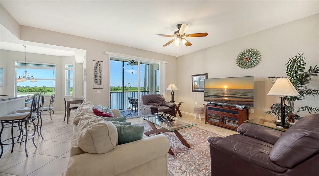 A living room features a sofa, leather chairs, a glass coffee table, and a balcony view — 7705 GRAND ESTUARY TRAIL UNIT 207, BRADENTON, FL