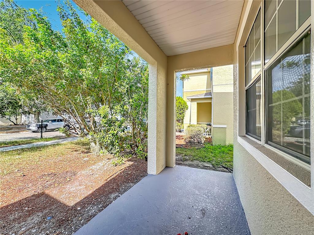 A covered concrete porch looks out toward a neighboring building and a tree-lined parking area — 1620 ATLANTIC DRIVE, RUSKIN, FL