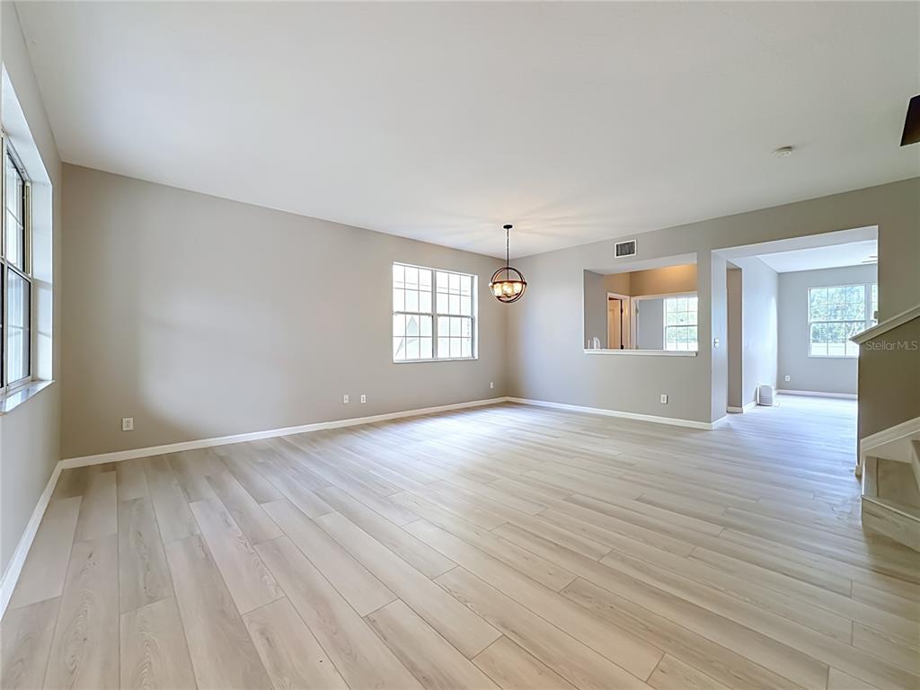 An empty living room features light wood-look flooring, neutral walls, and a modern pendant light — 1620 ATLANTIC DRIVE, RUSKIN, FL