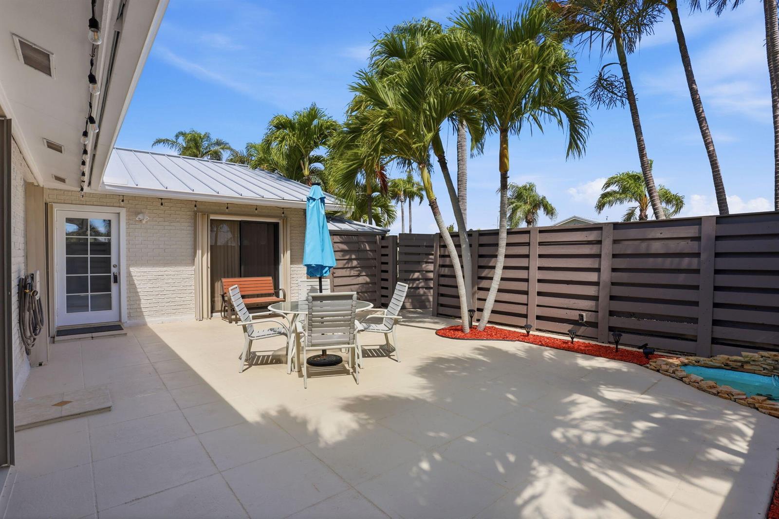 A patio features a dining set, a blue umbrella, palm trees, and a privacy fence — 1801 S Us Hwy 1 # 3a, Jupiter FL 33477, JUPITER, FL