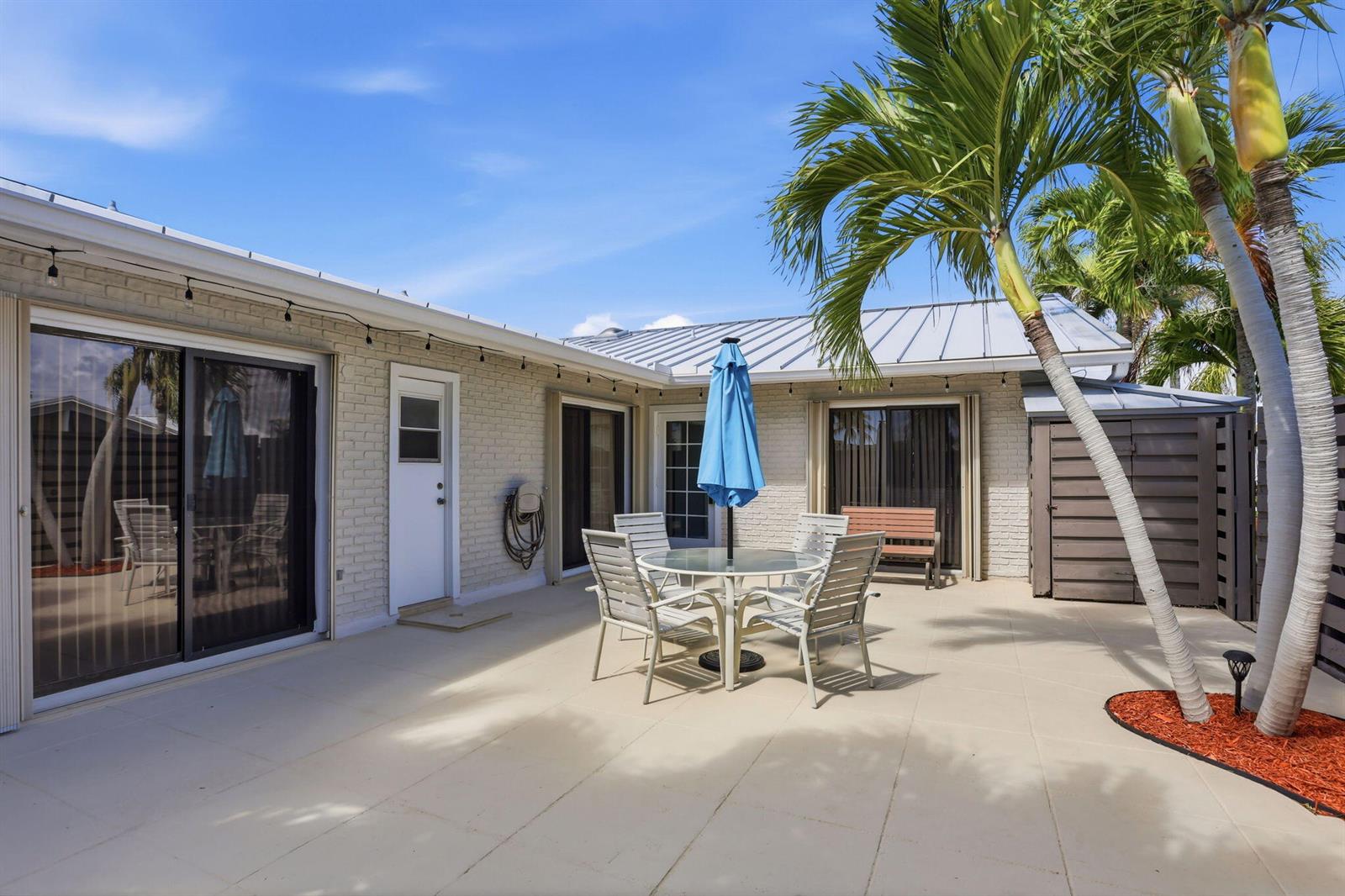 A paved patio features a dining set with a blue umbrella and palm trees — 1801 S Us Hwy 1 # 3a, Jupiter FL 33477, JUPITER, FL