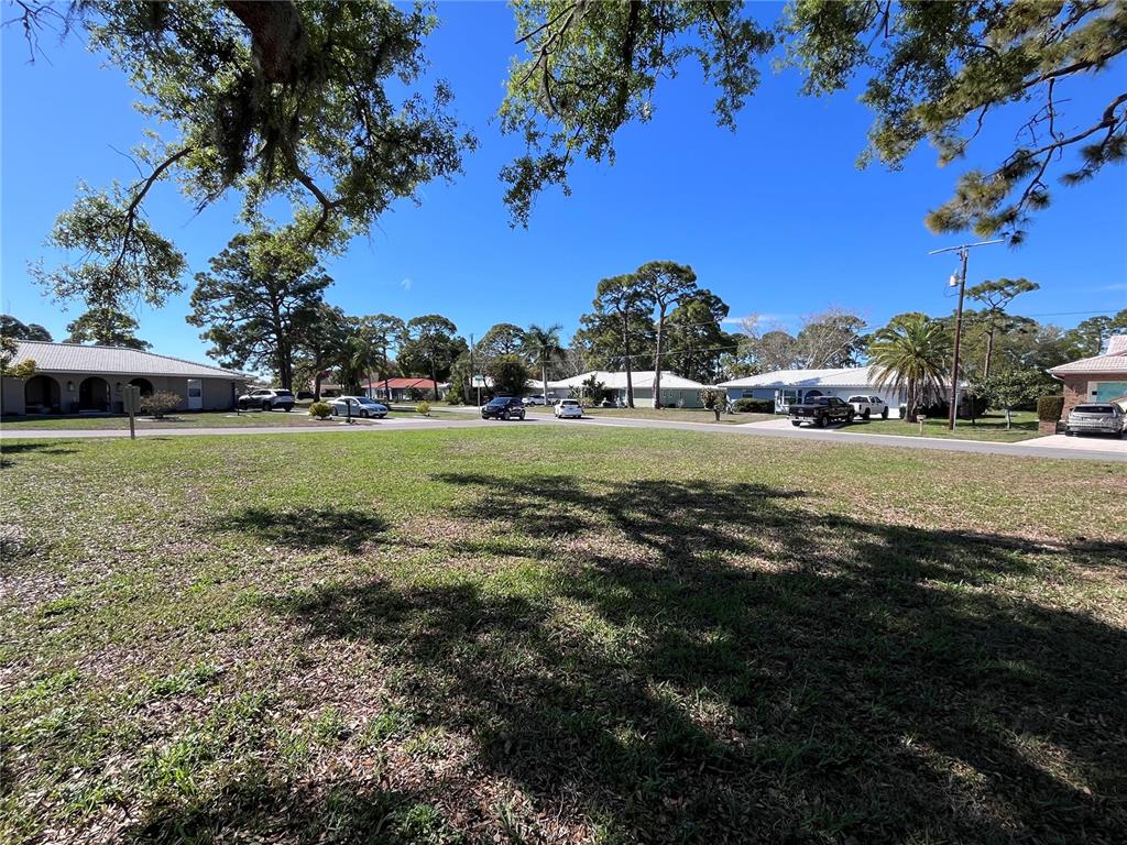 A grassy vacant lot sits in front of several single-story suburban houses under a blue sky — 618 RUBENS DRIVE UNIT 618, NOKOMIS, FL