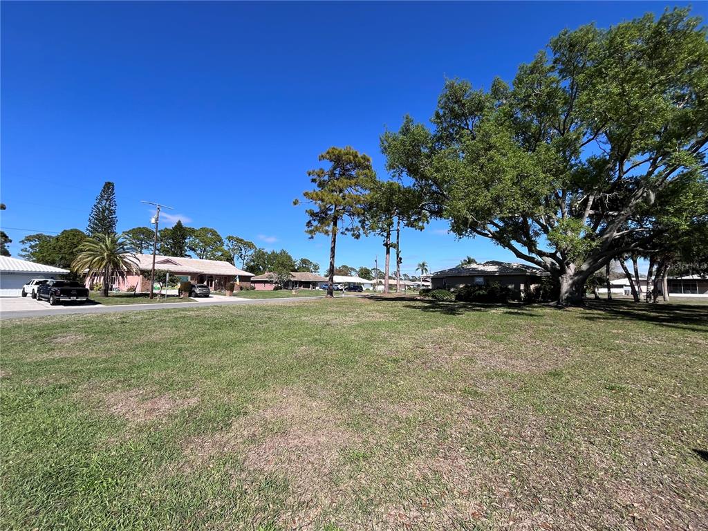 A grassy vacant lot sits in a residential neighborhood with mature trees and nearby houses — 618 RUBENS DRIVE UNIT 618, NOKOMIS, FL
