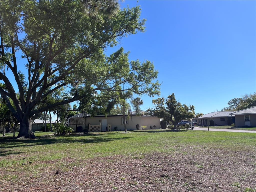 A large tree shades a tan house with a lawn in a residential neighborhood — 618 RUBENS DRIVE UNIT 618, NOKOMIS, FL