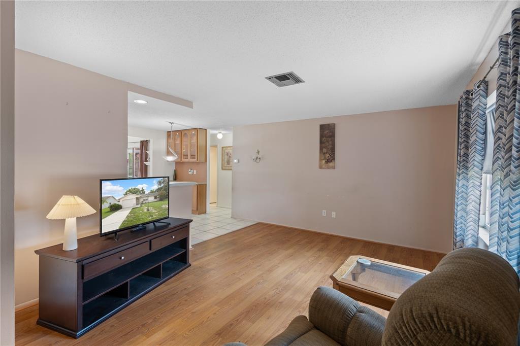 A living room with wood-look flooring, a television on a console, and an adjacent kitchen — 2234 MARINER BOULEVARD, SPRING HILL, FL