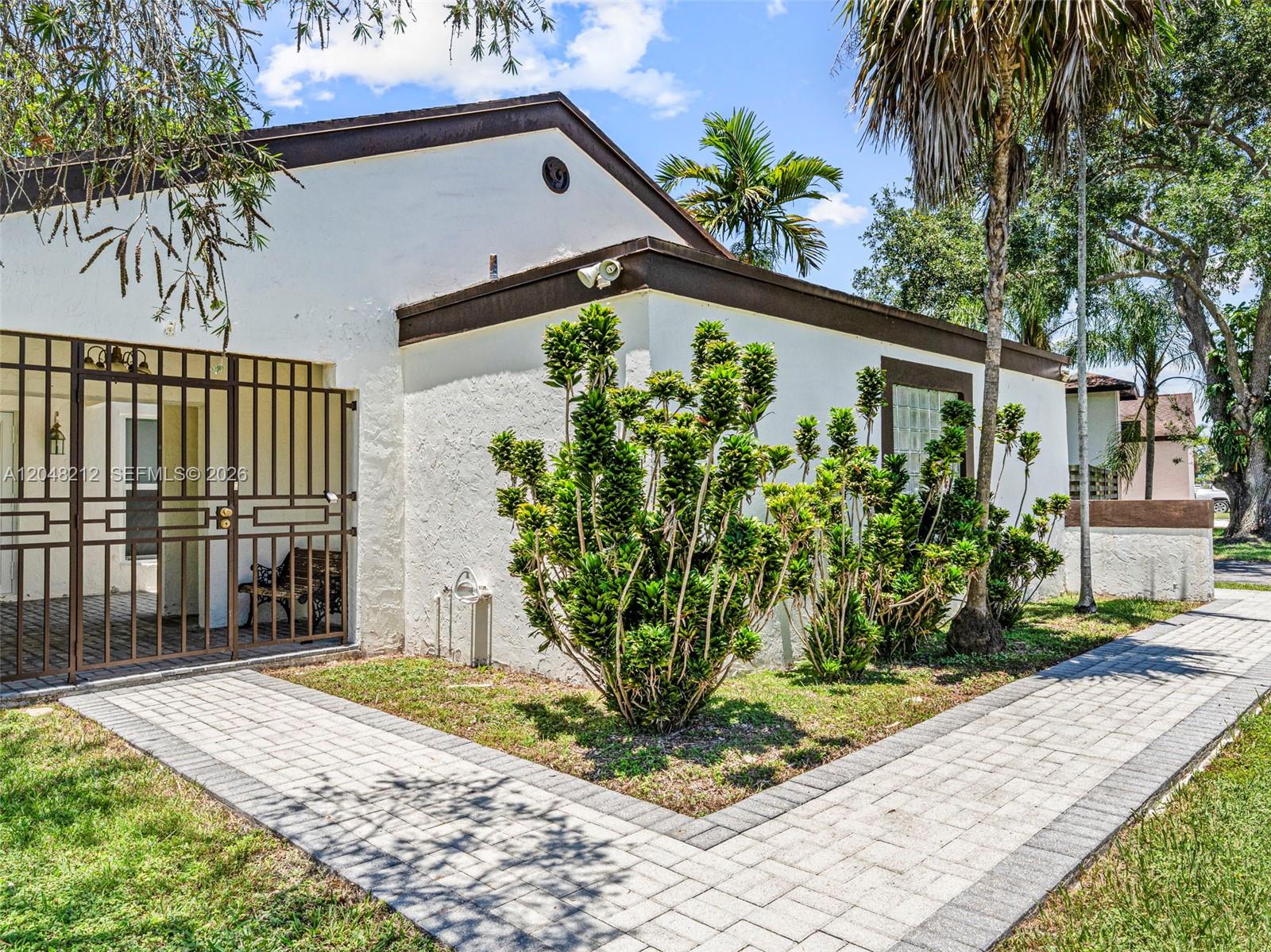 A white house exterior features a paved walkway, a metal security gate, and landscaping — 15491 SW 153rd St, Miami FL 33187, MIAMI, FL