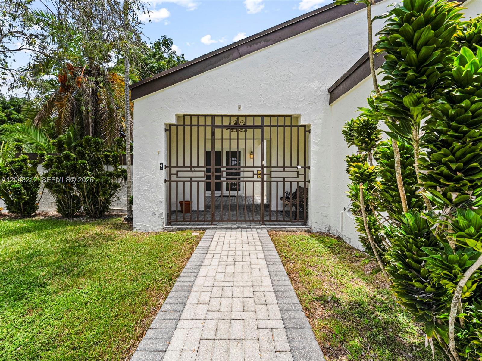 A paved walkway leads to a gated entryway of a white house with a brown roof — 15491 SW 153rd St, Miami FL 33187, MIAMI, FL