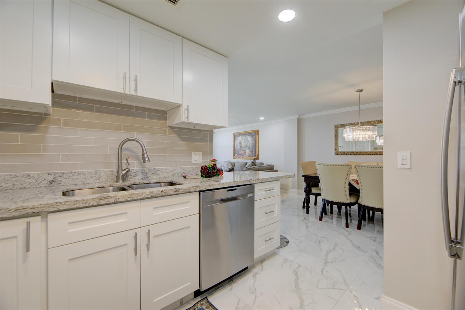 A modern kitchen with white cabinets, granite countertops, and stainless steel appliances overlooks a dining area — 305 N Pompano Beach Boulevard # 1007, Pompano Beach FL 33062, POMPANO BEACH, FL