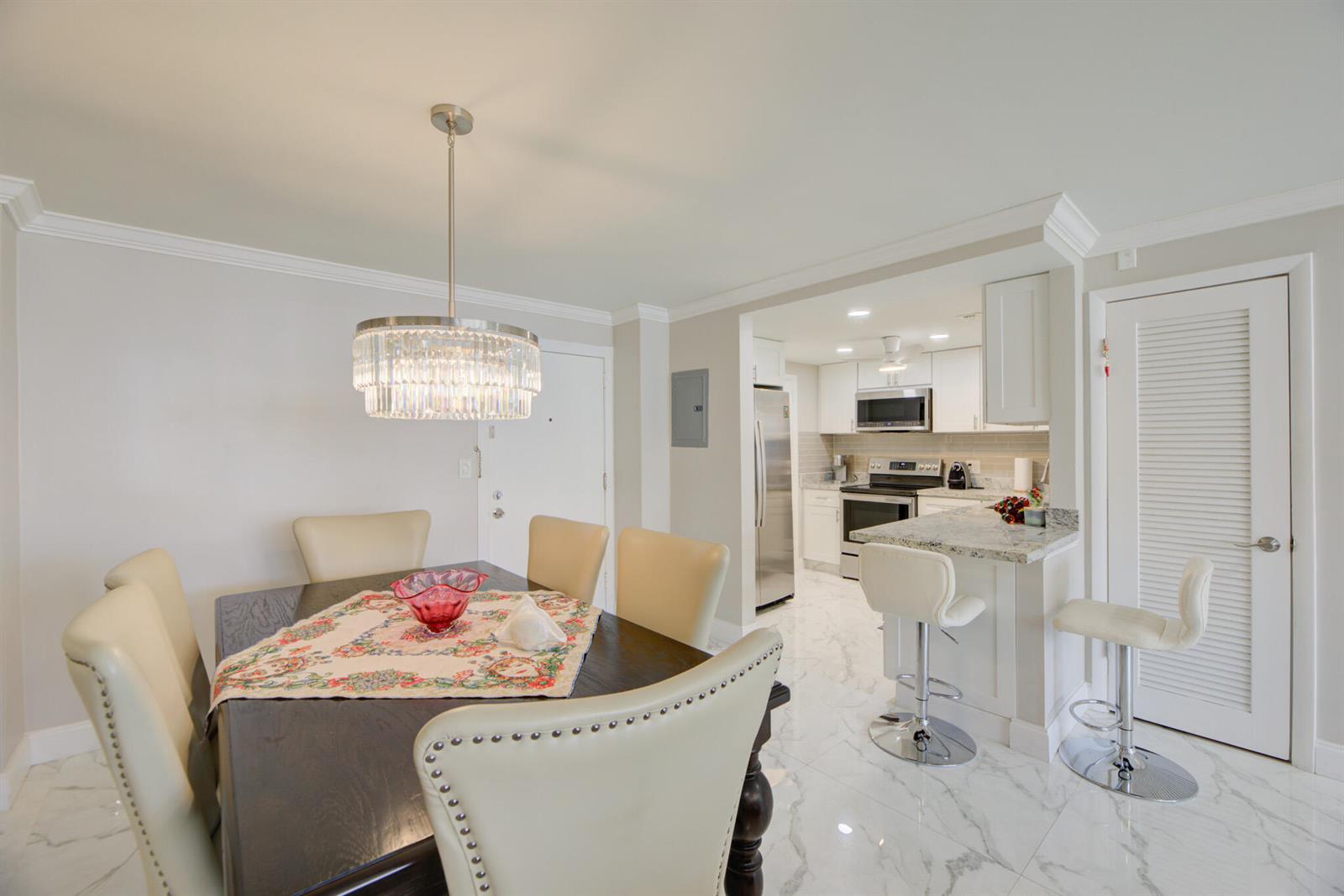 A dining area with a crystal chandelier and a kitchen with white cabinets and stools — 305 N Pompano Beach Boulevard # 1007, Pompano Beach FL 33062, POMPANO BEACH, FL