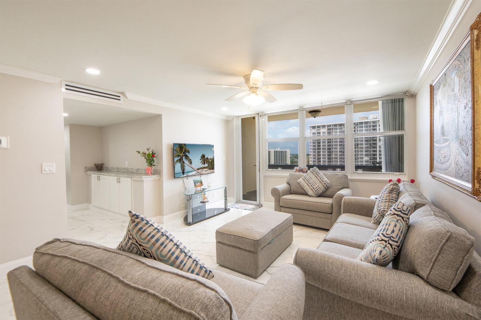 A living room with gray sofas, a television, marble floors, and a view of buildings — 305 N Pompano Beach Boulevard # 1007, Pompano Beach FL 33062, POMPANO BEACH, FL