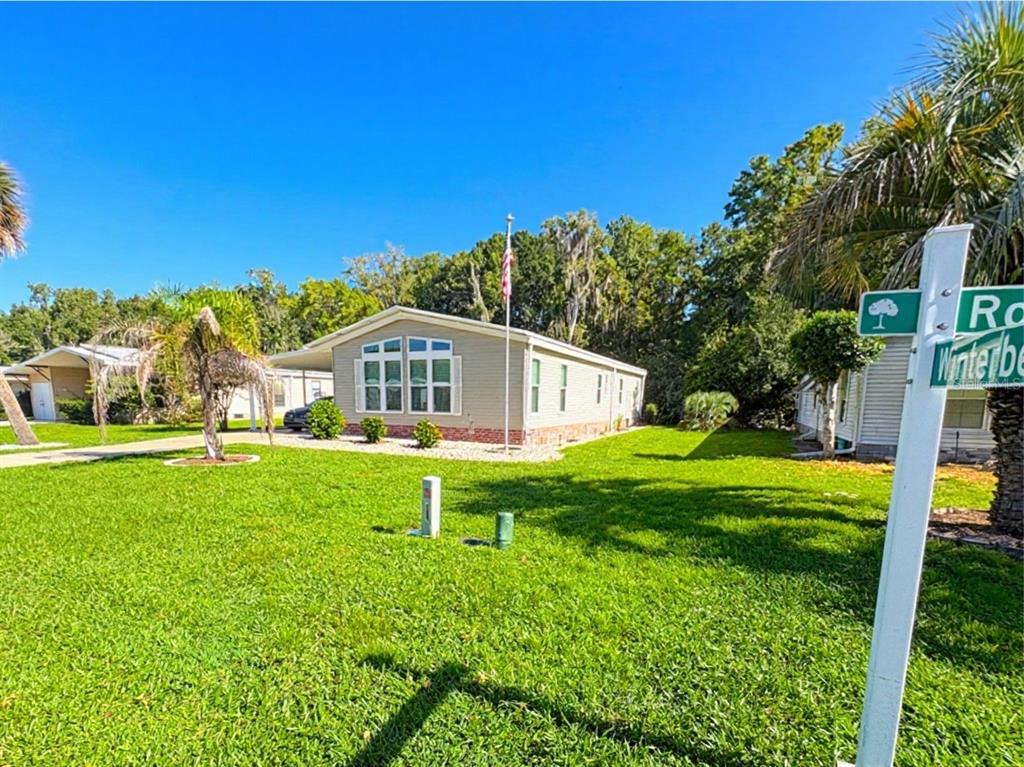 A single-story manufactured home with light siding and a brick base sits on a lawn — 601 ROBIN LANE, WILDWOOD, FL