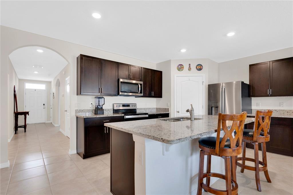 A kitchen features dark wood cabinets, granite countertops, a center island, and stainless steel appliances — 1735 PARK SIDE AVENUE, KISSIMMEE, FL
