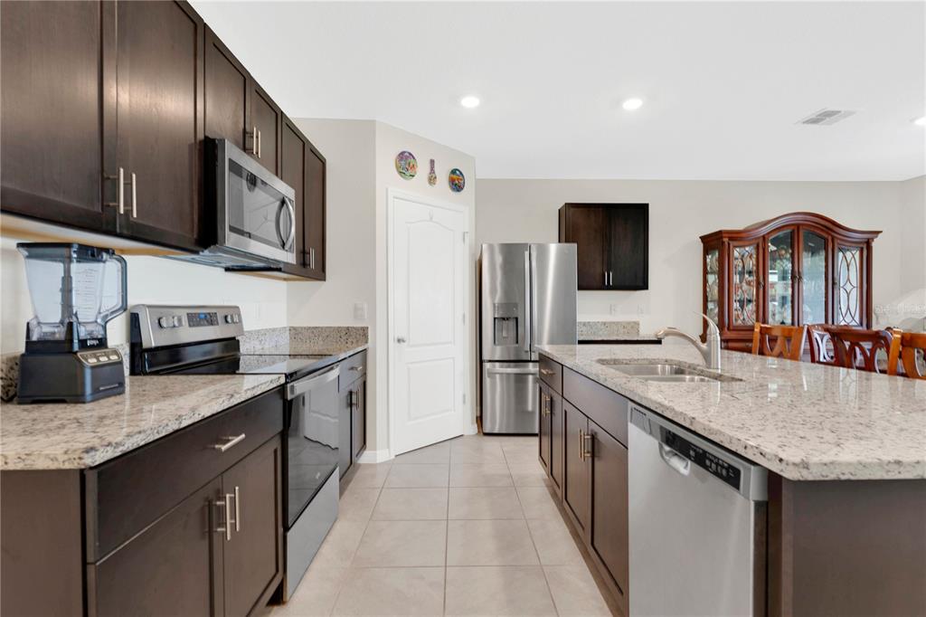 A kitchen features dark wood cabinets, granite countertops, stainless steel appliances, and a central island — 1735 PARK SIDE AVENUE, KISSIMMEE, FL