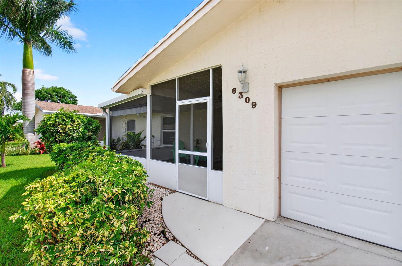 A white house exterior features a screened-in porch, a garage door, and a landscaped yard — 6309 Dusenburg Road, Delray Beach FL 33484, DELRAY BEACH, FL