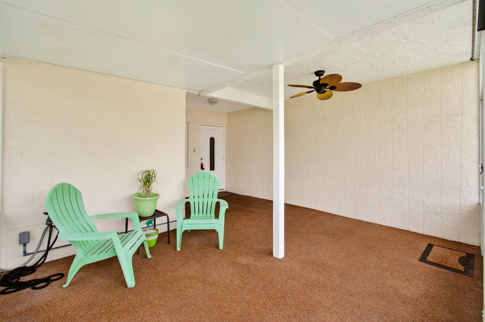 A covered patio features a brown textured floor, two light green chairs, and a ceiling fan — 6309 Dusenburg Road, Delray Beach FL 33484, DELRAY BEACH, FL