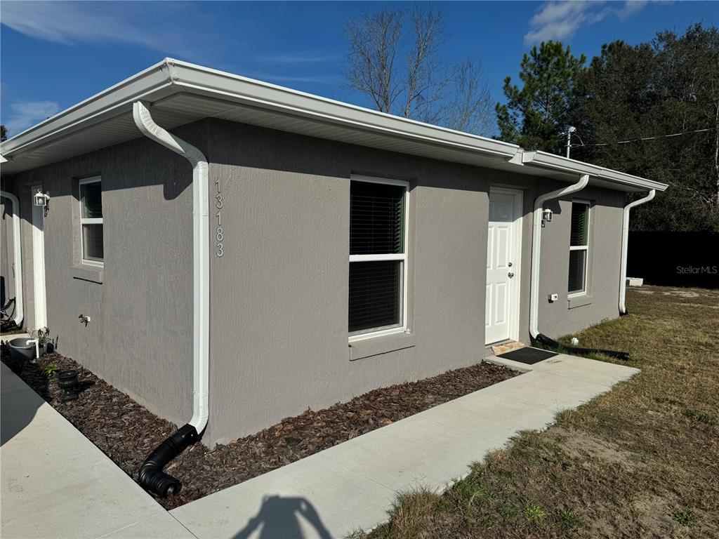 A gray stucco exterior of a single-story house with white trim and a concrete walkway — 13183 SW 113TH PLACE, DUNNELLON, FL