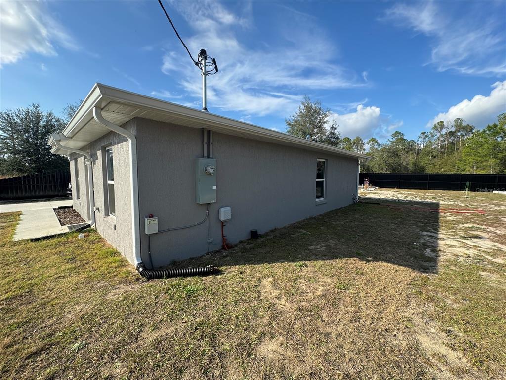 The exterior side of a gray stucco house features an electrical meter and utility boxes — 13183 SW 113TH PLACE, DUNNELLON, FL