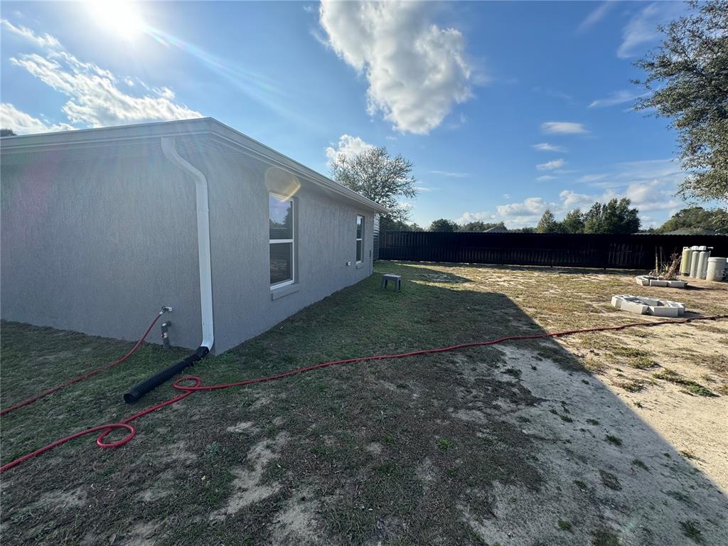 The exterior side of a gray stucco house features a downspout and a fenced yard — 13183 SW 113TH PLACE, DUNNELLON, FL