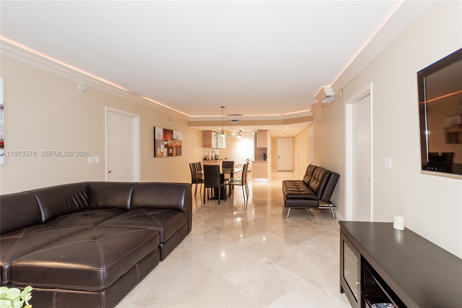 A living room with a dark leather sectional, dining area, and light tile flooring — 1800 S OCEAN DR # 3803, Hallandale Beach FL 33009, HALLANDALE BEACH, FL
