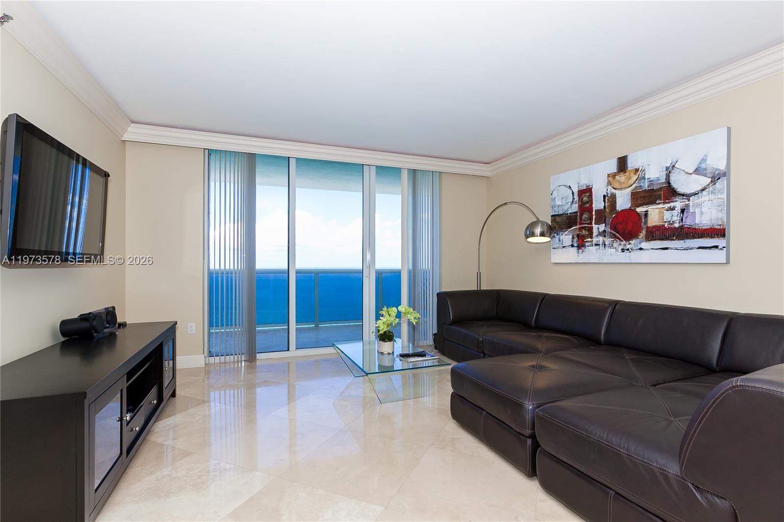 A living room features a dark leather sectional, glass coffee table, and ocean view balcony — 1800 S OCEAN DR # 3803, Hallandale Beach FL 33009, HALLANDALE BEACH, FL
