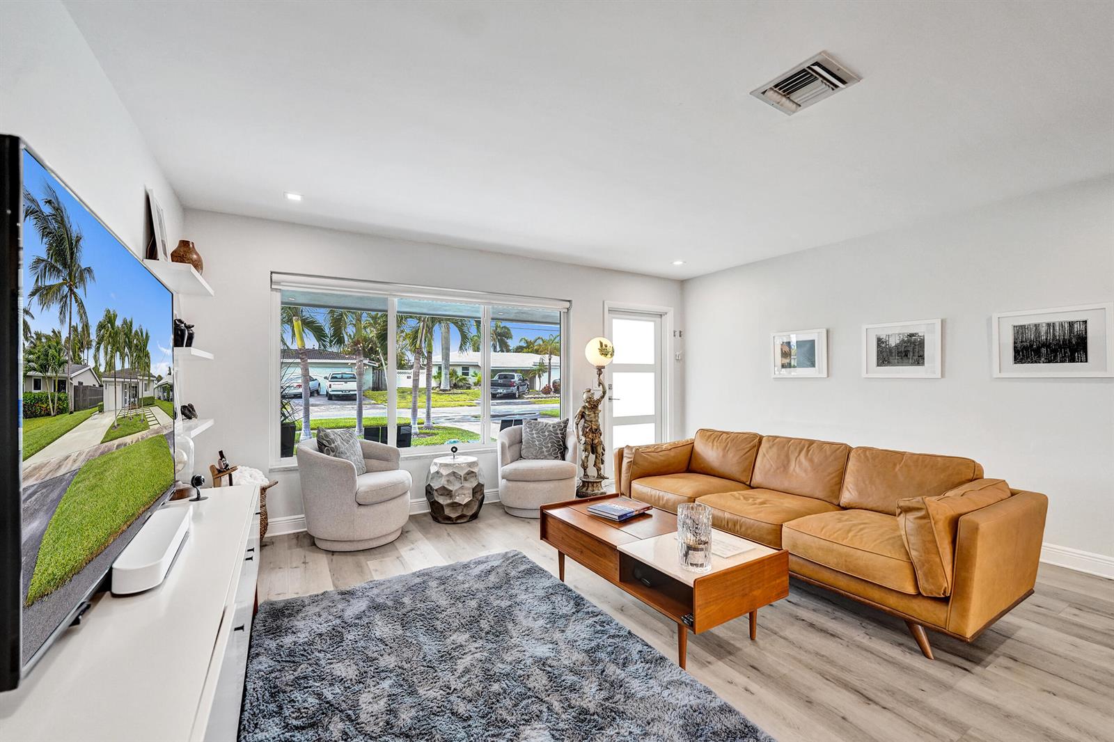 A living room features a tan leather sofa, two gray armchairs, and a large television — 381 SE 3rd Street, Pompano Beach FL 33060, POMPANO BEACH, FL