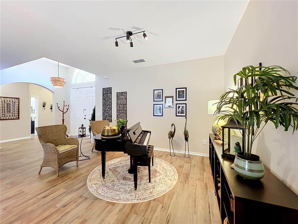 A living area features a black piano on a round rug, wicker chairs, and decor — 527 AZALEA BLOOM DRIVE, APOPKA, FL