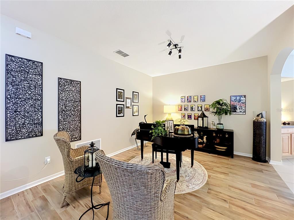 A living room features a grand piano, wicker chairs, and wall art on wood-look flooring — 527 AZALEA BLOOM DRIVE, APOPKA, FL