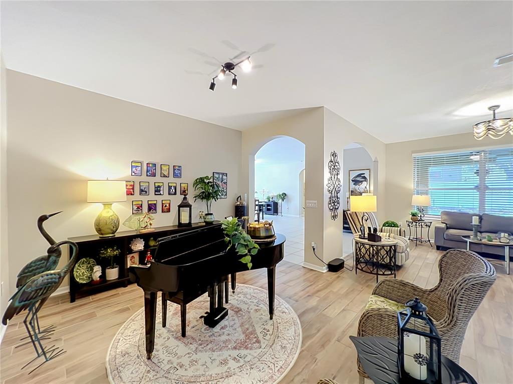 A living room features a black grand piano, wood-look flooring, and an arched entryway — 527 AZALEA BLOOM DRIVE, APOPKA, FL