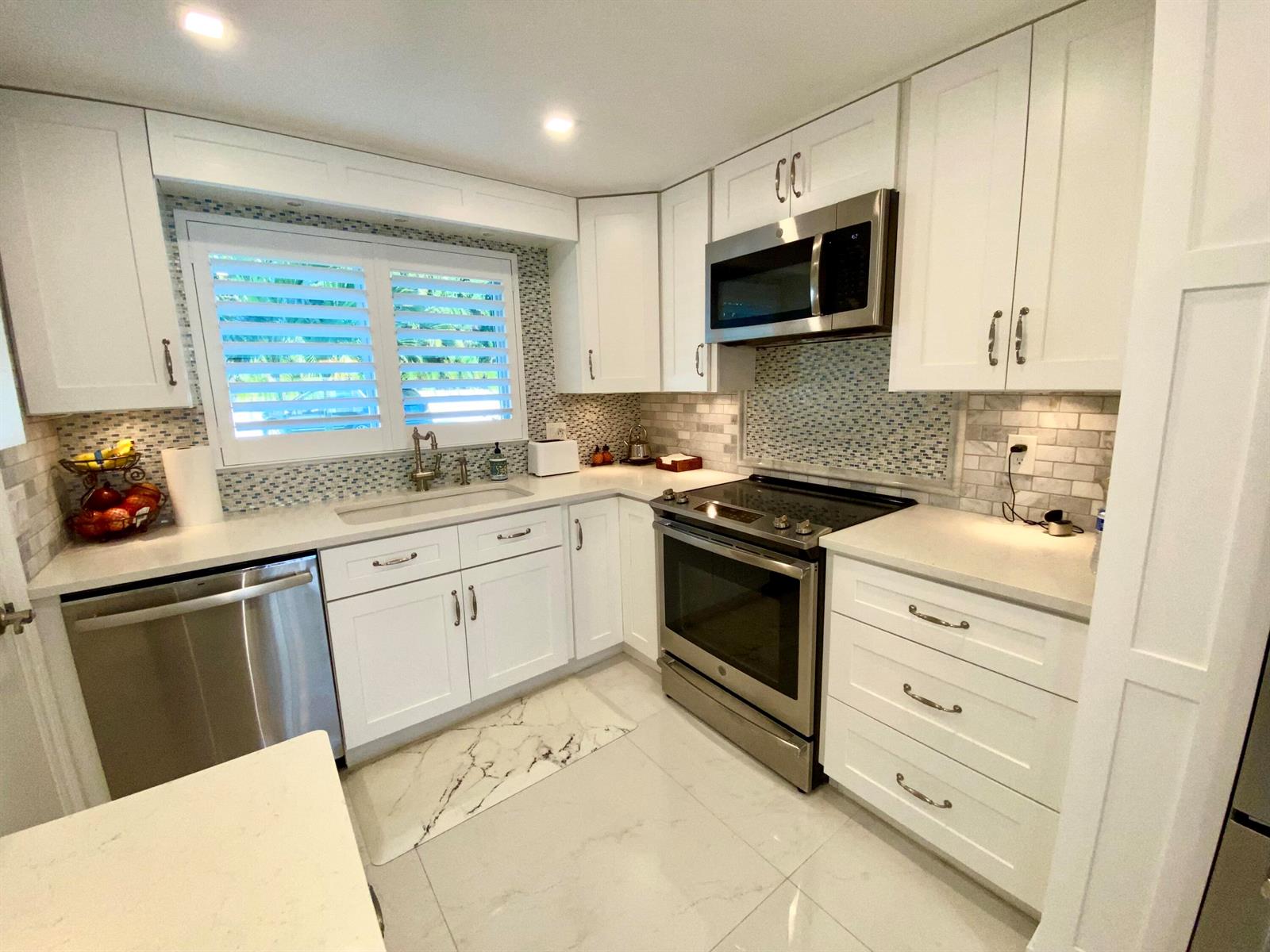 A bright kitchen features white cabinets, stainless steel appliances, and a mosaic tile backsplash — 331 Tequesta Drive # 118, Tequesta FL 33469, TEQUESTA, FL