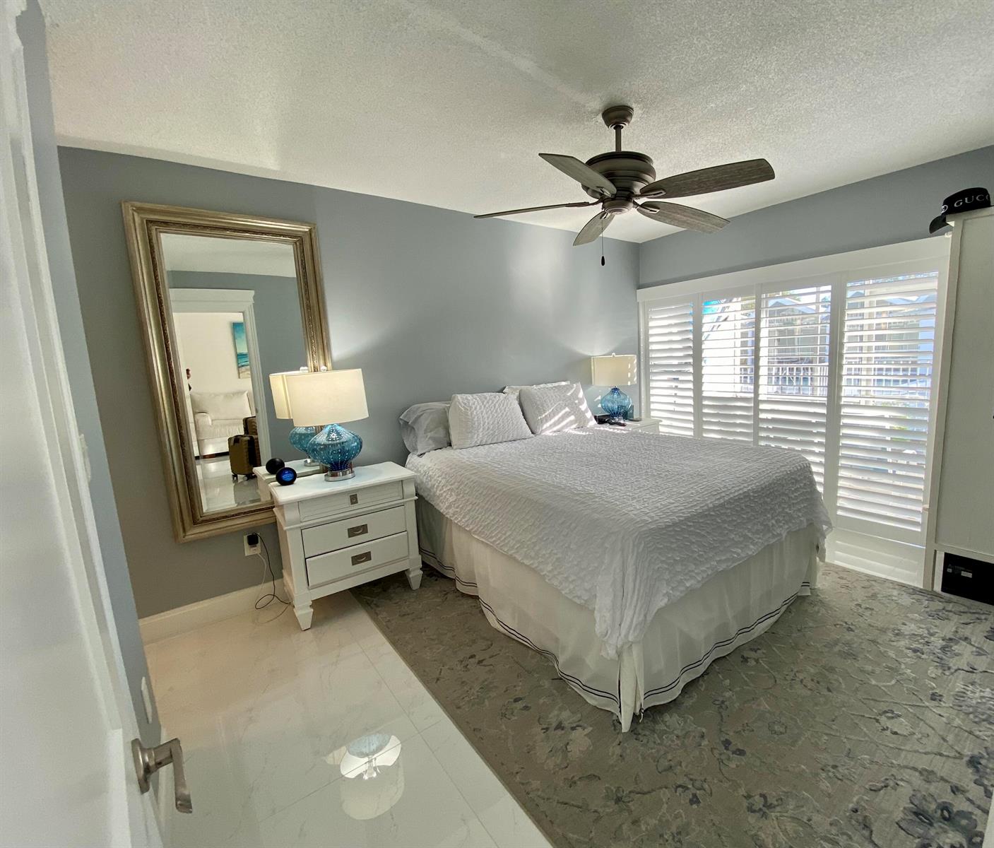 A bedroom features a bed with white bedding, a large floor mirror, and plantation shutters — 331 Tequesta Drive # 118, Tequesta FL 33469, TEQUESTA, FL
