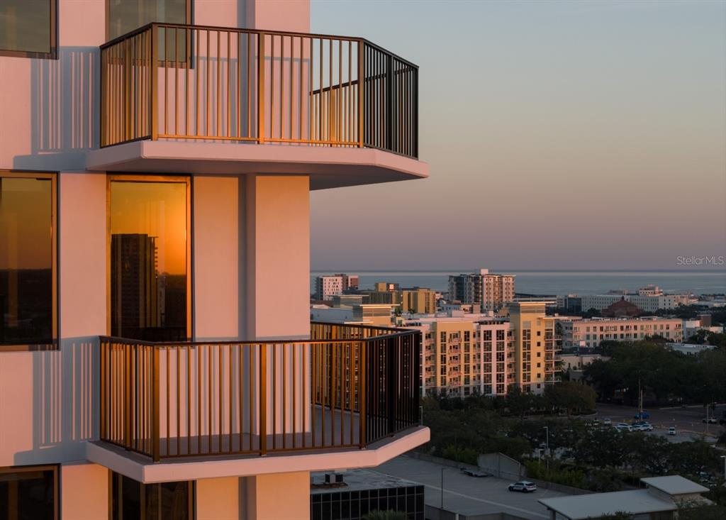 Two stacked balconies with black railings overlook a city skyline and the ocean at sunset — 1000 1ST AVENUE N UNIT C1, ST PETERSBURG, FL