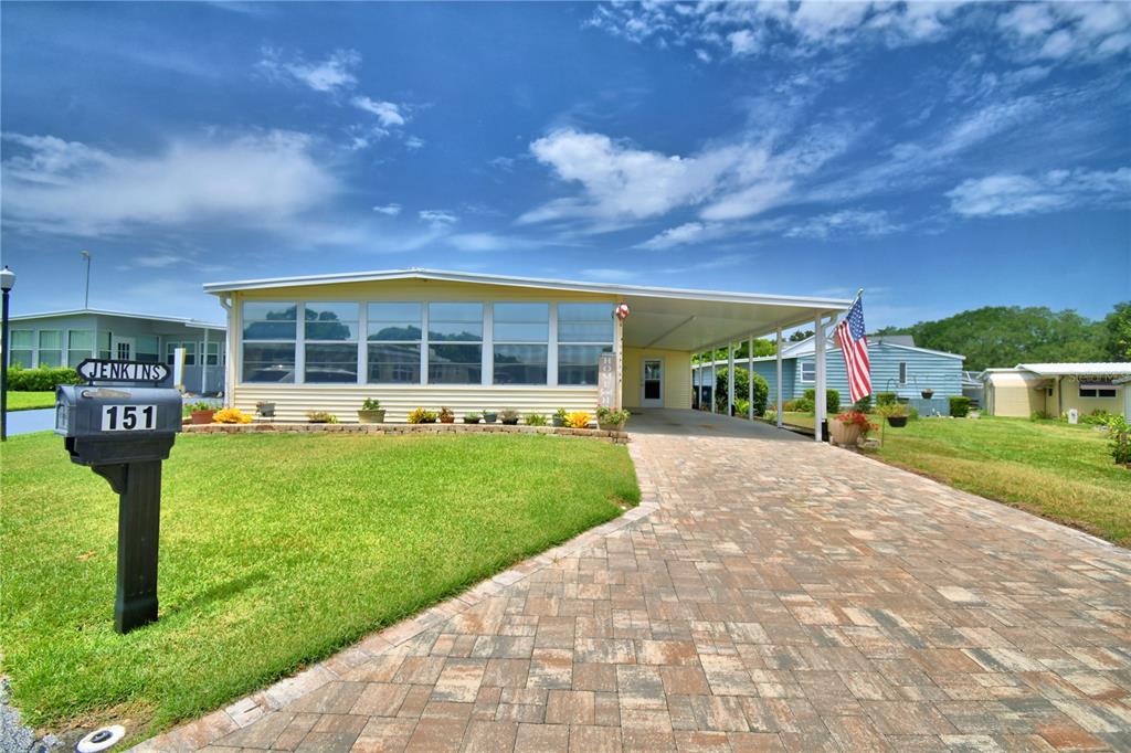 A yellow manufactured home features a paved driveway, a carport, and a front lawn — 151 HOLIDAY LANE, AUBURNDALE, FL