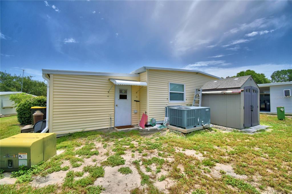 The exterior of a yellow mobile home features a white door, HVAC unit, and shed — 151 HOLIDAY LANE, AUBURNDALE, FL