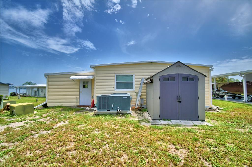The exterior of a yellow house features a storage shed, an AC unit, and a door — 151 HOLIDAY LANE, AUBURNDALE, FL