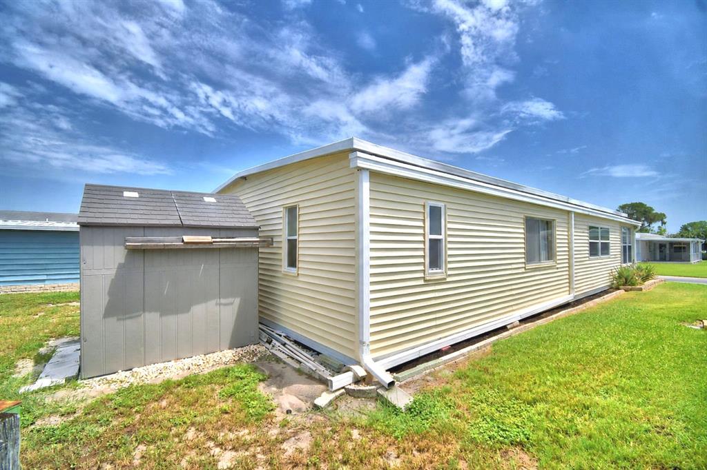 The exterior of a yellow mobile home features a gray storage shed and white trim — 151 HOLIDAY LANE, AUBURNDALE, FL