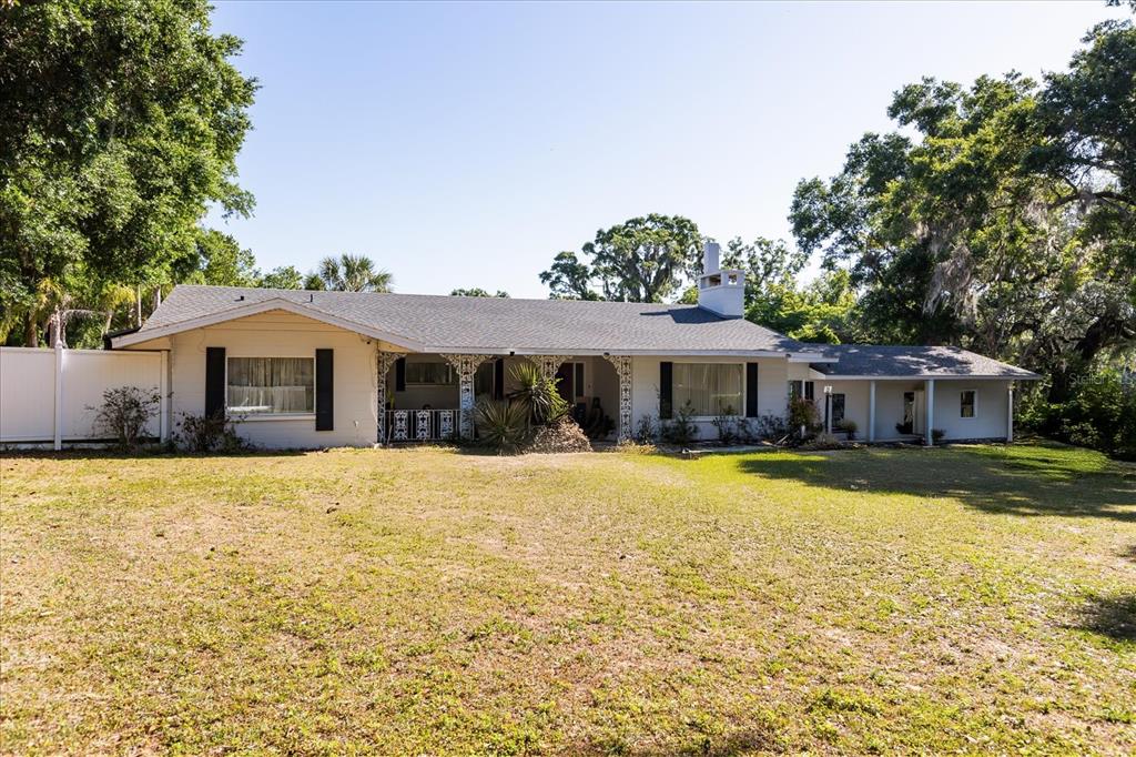 A single-story white house with a gray shingled roof and decorative metal porch supports — 1505 E CROOKED LAKE DRIVE, EUSTIS, FL