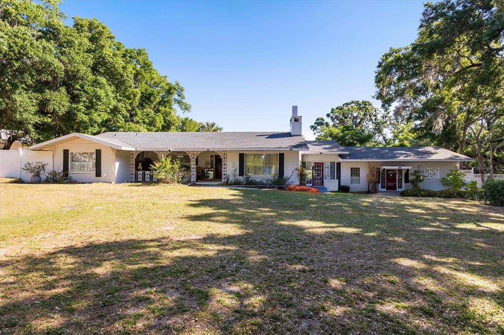 A single-story white house with a gray shingled roof sits behind a large grassy lawn — 1505 E CROOKED LAKE DRIVE, EUSTIS, FL
