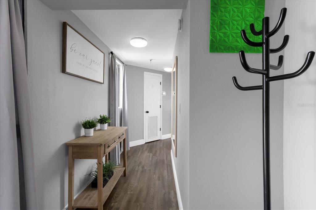 A hallway features wood-look flooring, a console table with plants, and a coat rack — 6165 CARRIER DRIVE UNIT 2901, ORLANDO, FL