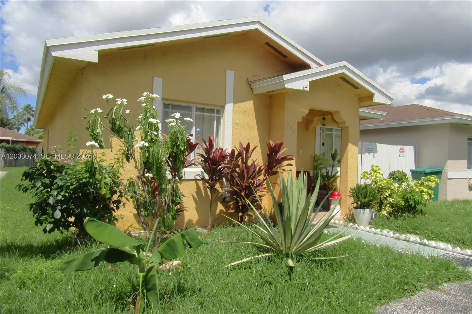 A yellow single-story house features a front porch, a small yard, and various tropical plants — 942 SW 8th Pl, Florida City FL 33034, FLORIDA CITY, FL