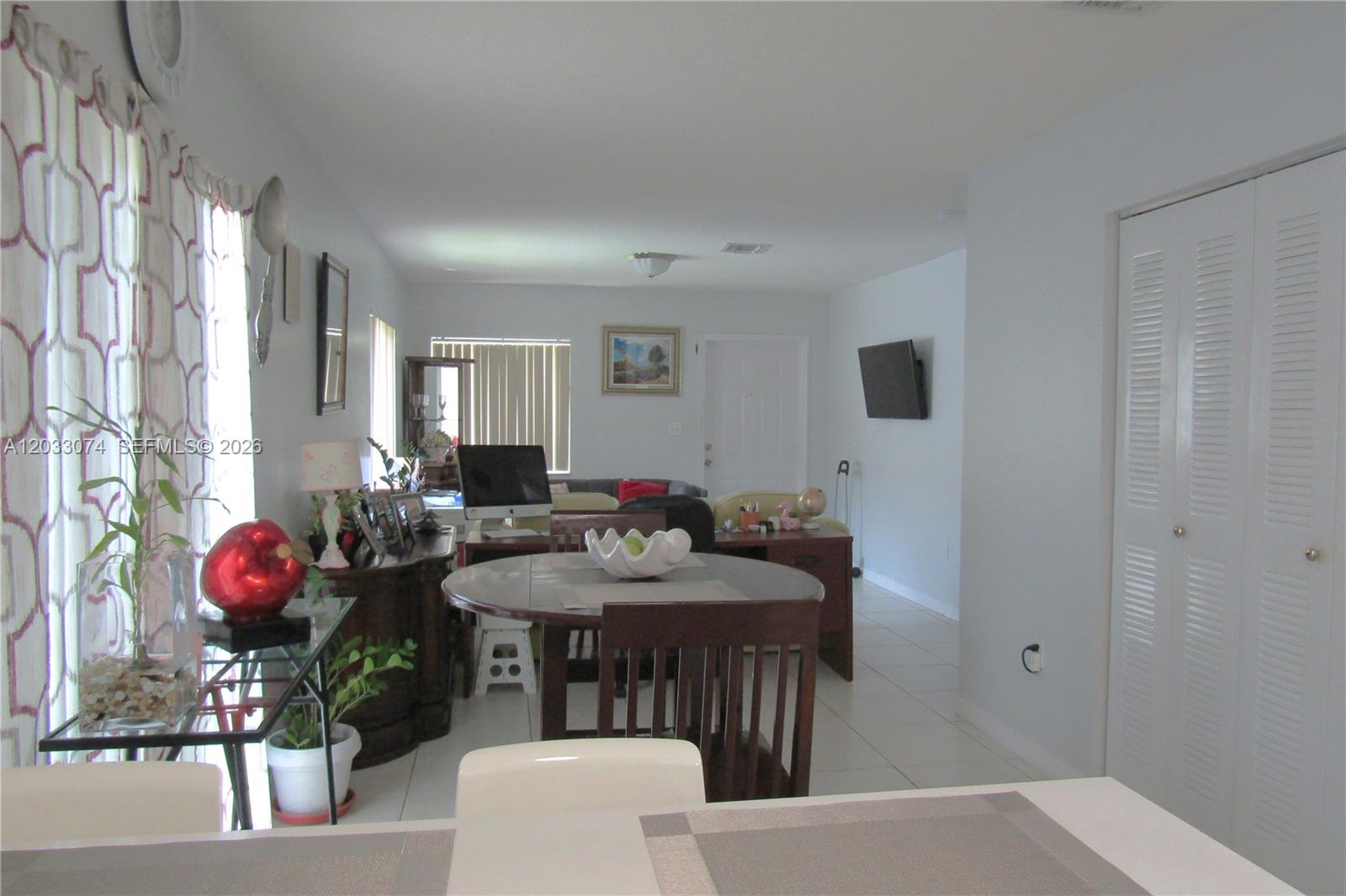 This open-concept living and dining area features white tile flooring and a round wooden table — 942 SW 8th Pl, Florida City FL 33034, FLORIDA CITY, FL